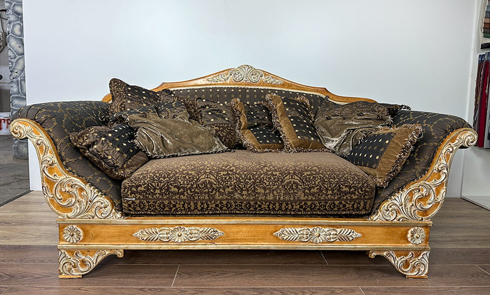 Роскошный винтажный диван с резными деревянными элементами, обитыми тёмной тканью с золотым узором со следами износа под замену обивки